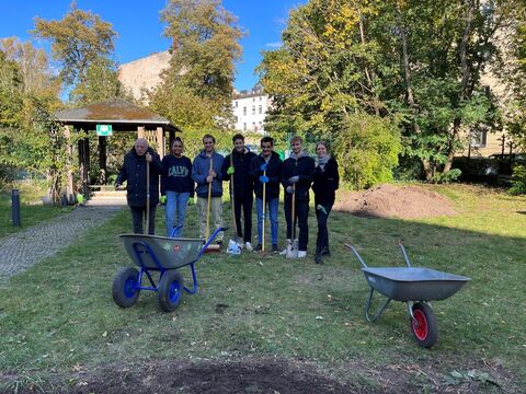 Freiwillige und Klient:innen beim Arbeitseinsatz mit Schaufel und Schubkarren im Garten der Wohnstätte 5 in Spandau.